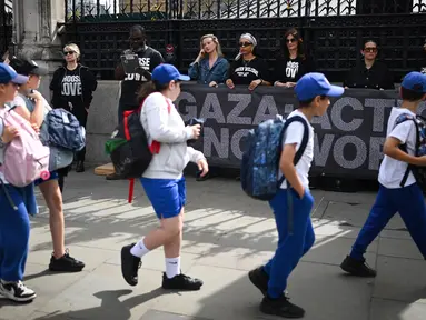 Anak-anak sekolah berjalan melewati aksi protes yang dilakukan oleh organisasi non-pemerintah Choose Love Europe di luar Gedung Parlemen di London, Inggris pada 29 Mei 2025. (Justin TALLIS/AFP)