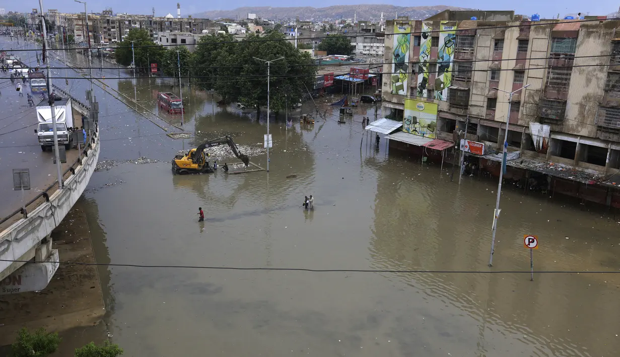 Orang-orang melintasi daerah banjir setelah hujan deras di Karachi, Pakistan, Minggu, (26/7/2020). Banjir melumpuhkan arus lalu lintas salah satu ruas jalan di Karachi. (AP Photo/Fareed Khan)