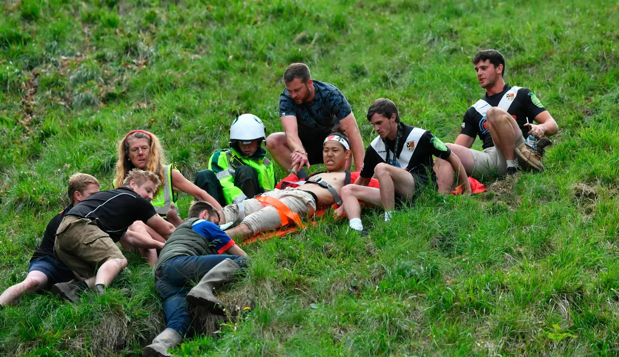 Seorang pria ditandu setelah ambil bagian dalam kompetisi Cheese Rolling (mengejar keju) di Bukit Cooper, Gloucestershire, Inggris, Senin (27/5/2019). Festival ini sebenarnya cukup berbahaya, sehingga tidak heran jika setiap tahun selalu ada korban yang luka. (Ben Birchall/PA via AP)