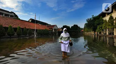 Siswi berjalan melewati banjir yang menggenangi halaman  sekolah di SMAN 4 Tangsel, Pondok Ranji, Tangerang Selatan, Banten, Selasa (14/6/2022). Tiga  pekan lebih banjir merendam lapangan sekolah itu dikarenakan tertutupnya saluran air oleh sampah yang berasal dari tempat pembuangan sampah (TPS) ilegal. (merdeka.com/Arie Basuki)