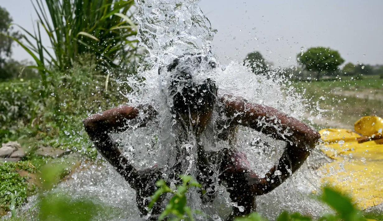 Seorang pria mandi di bawah air yang mengalir dari pipa di sepanjang dataran Yamuna pada suatu sore di New Delhi pada tanggal 29 Mei 2024. (Arun SANKAR/AFP)