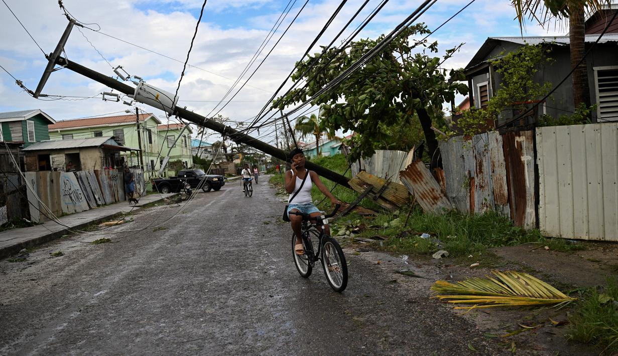 Orang-orang bersepeda di jalan dengan tiang listrik tumbang setelah Badai Lisa di Belize City, Belize, 3 November 2022. Badai Tropis Lisa menyebabkan banjir dan membuat sebagian negara itu menjadi gelap gulita. (Johan ORDONEZ/AFP)