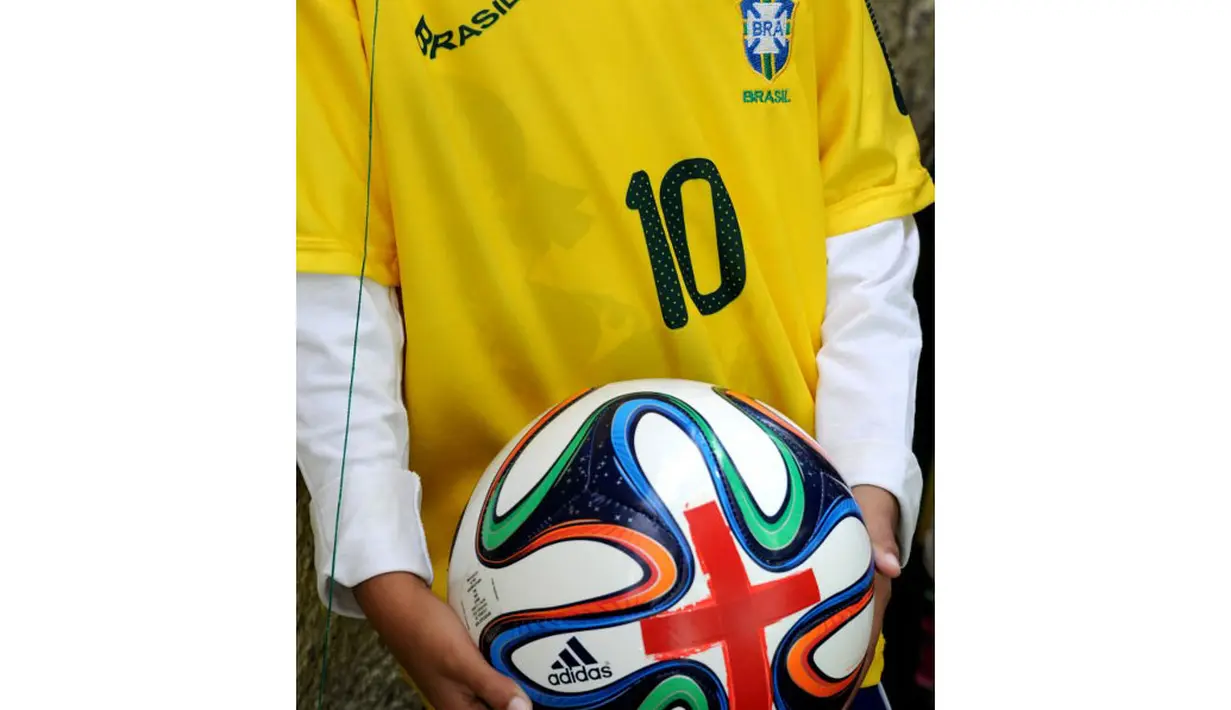 Seorang anak memperlihatkan replika bola yang akan digunakan saat Piala Dunia 2014 yang diberi tanda palang merah, (10/5/2014). (AFP PHOTO/Tasso Marcelo) 