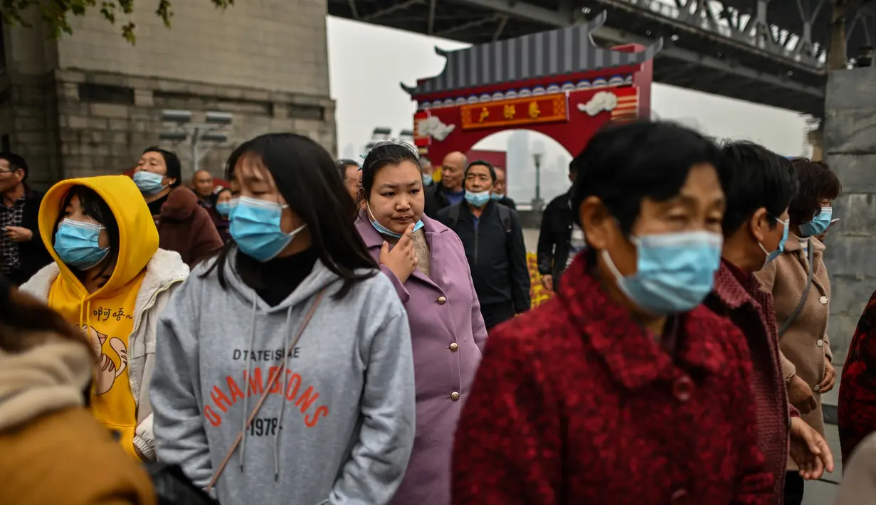 Turis domestik dari provinsi Henan yang mengenakan masker wajah mengunjungi daerah di sebelah Sungai Yangtze di Wuhan (20/11/2020). Dari total 50.340 kasus yang positif di Wuhan, 3.869 orang telah meninggal dunia akibat Covid-19 dan yang sembuh 46.471 orang. (AFP/Hector Retamal)