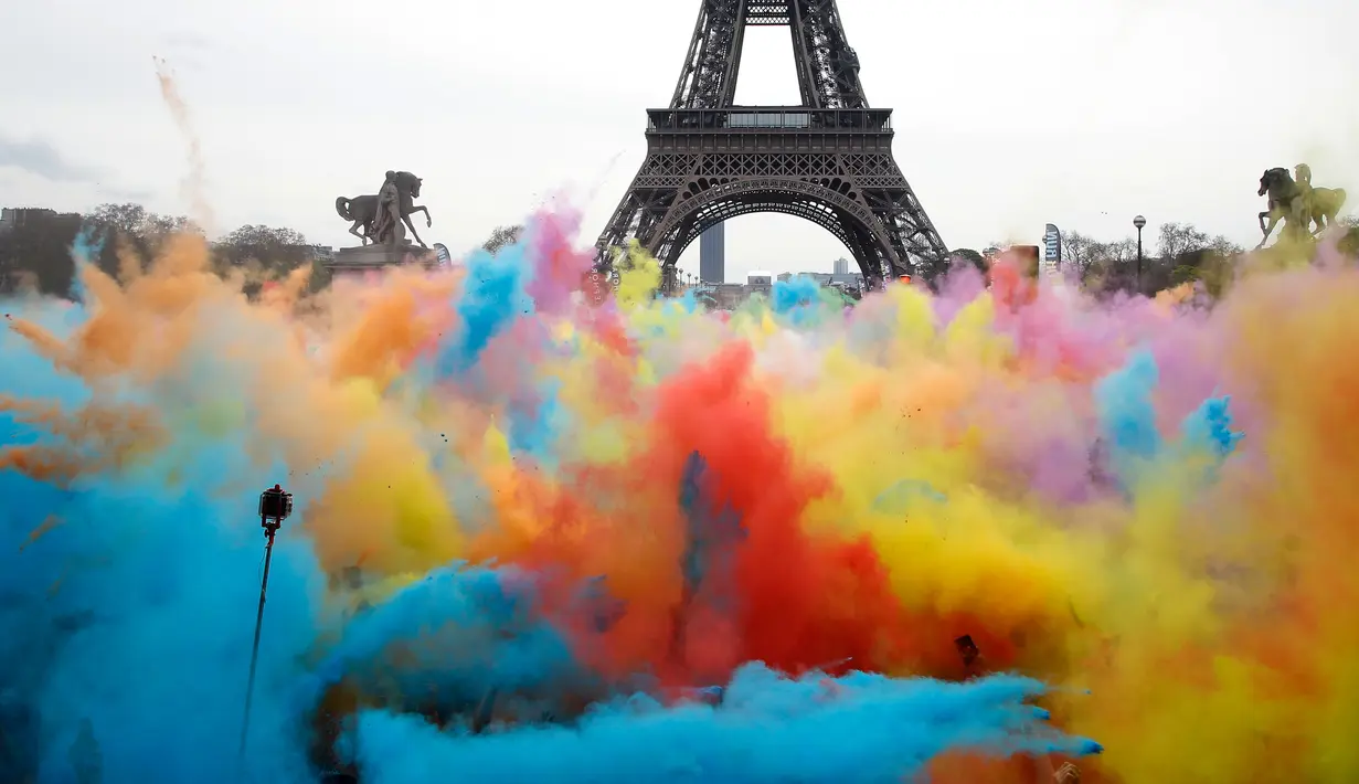 Pemandangan ketika sejumlah orang melempar bubuk berwarna saat merayakan akhir perlombaan Color Run 2018 di depan Menara Eiffel di Paris, Prancis (15/4). Dengan acara ini sekitar Menara Eiffel terlihat berwarna-warni. (AP/Thibault Camus)