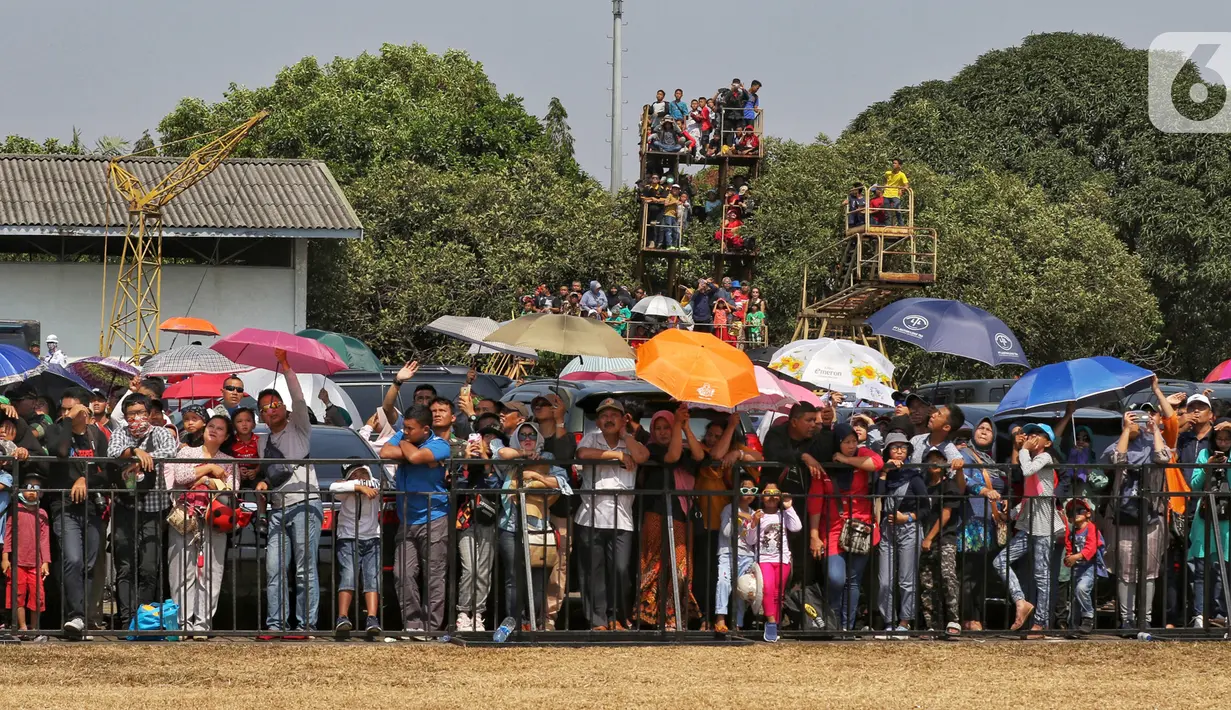 Sejumlah warga mengenakan payung saat menyaksikan perayaan HUT ke-74 TNI di Lanud Halim Perdanakusuma, Jakarta Timur, Sabtu (5/10/2019). Warga rela panas-panasan dan berdesak-desakan untuk menyaksikan perayaan HUT ke-74 TNI. (Liputan6.com/JohanTallo)
