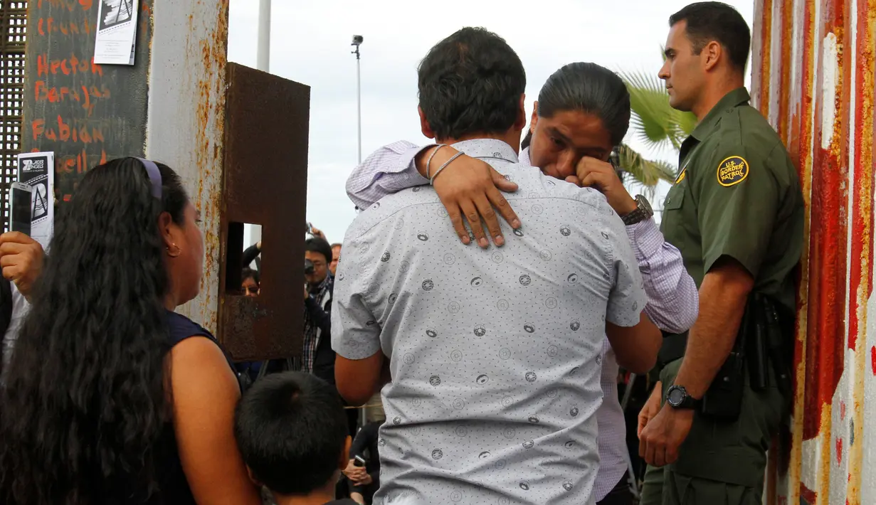 Seorang pria menangis sambil memeluk keluarganya di depan gerbang perbatasan Meksiko dan Amerika Serikat ,Tijuana, Meksiko (19/11). Untuk memperingati Hari Anak Sedunia, petugas membolehkan imigran Meksiko bertemu dengan keluarganya.(Reuters/Jorge Duenes)