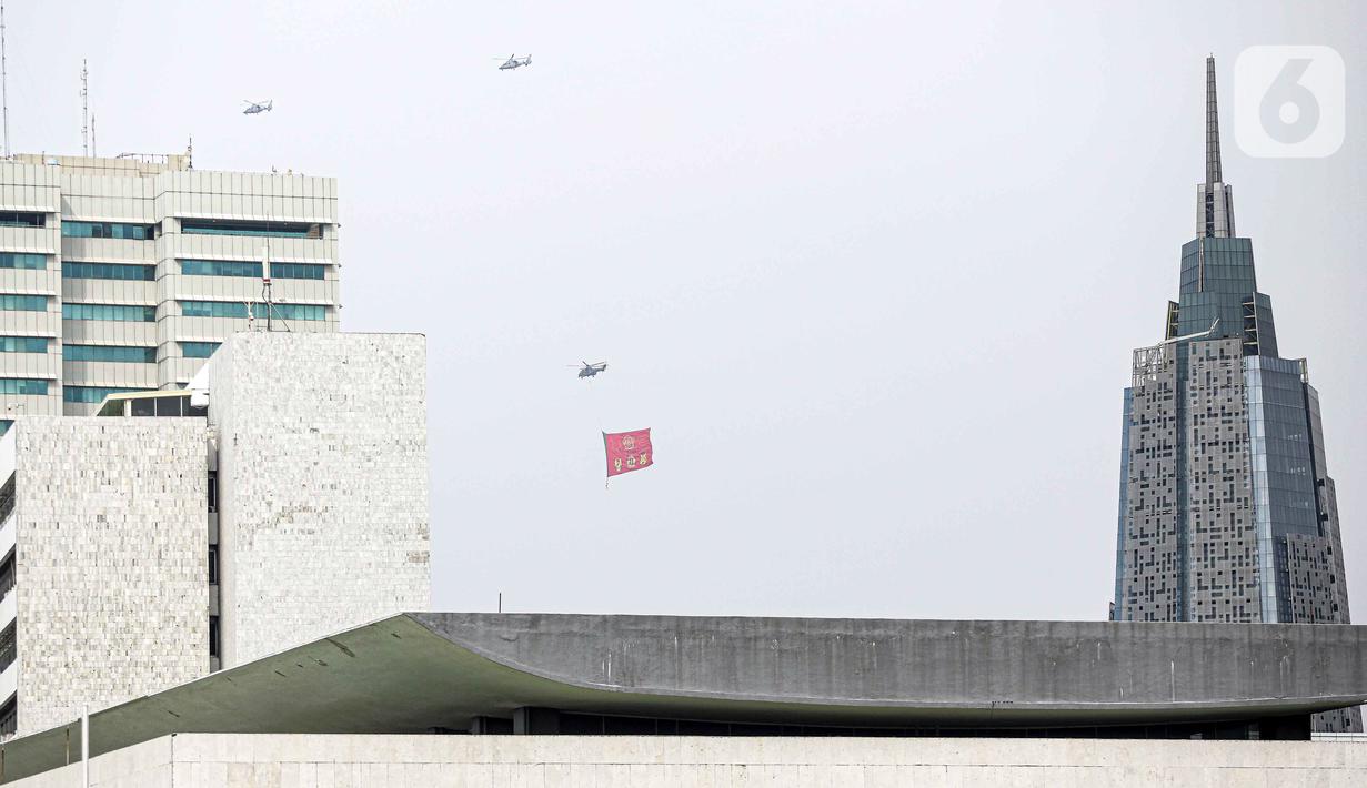 Helikopter TNI AU mengibarkan bendera Trimatra raksasa di kawasan Gedung DPR RI, Jakarta, Selasa (5/10/2021). Bendera raksasa ini dikibarkan dari timur ke barat langit Jakarta dalam rangka memperingati Hut ke-76 TNI. (Liputan6.com/Faizal Fanani)