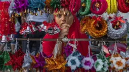 Seorang gadis penjual suvenir Natal menunggu pembeli di Mumbai, India, Selasa (20/12/2022). Jelang puncak perayaan Natal, warga Mumbai mulai ramai berburu ornamen dan aksesoris Natal untuk menyambut dan memeriahkan perayaan untuk umat kristiani tersebut. (AP Photo/Rafiq Maqbool)