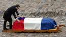 Presiden Prancis Emmanuel Macron meletakkan tangannya di peti jenazah Letnan Kolonel Arnaud Beltrame, setelah secara anumerta memberinya penghargaan perwira tertinggi  dalam upacara nasional di Hotel des Invalides, Paris, Rabu (28/3). (AP/Christophe Ena)