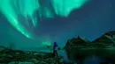 Seorang surfer membawa papannya melihat Cahaya Utara atau aurora borealis di Utakleiv, Norwegia utara (9/3). (AFP/Olivier Morin)