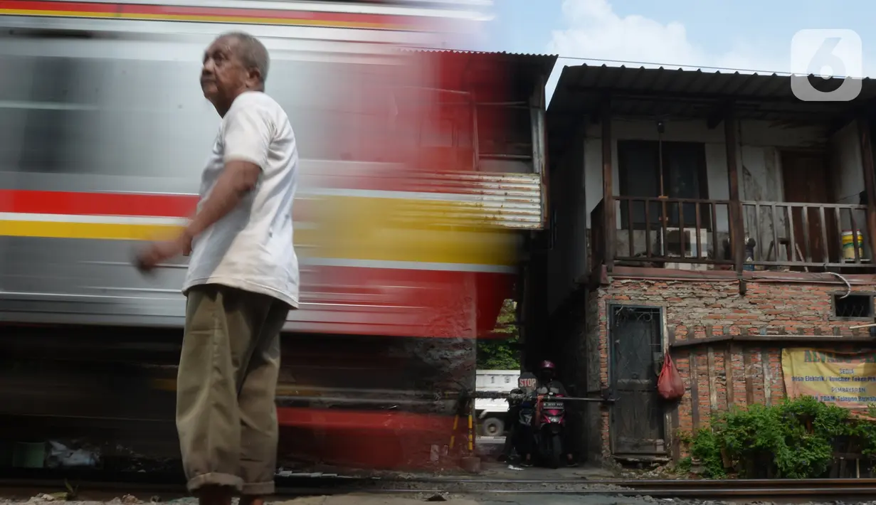 Penjaga perlintasan kereta api tanpa palang pintu, Wandi, berdiri tepat di samping perlintasan di Kawasan Petamburan, Jakarta, Jumat (4/6/2021). Di usianya yang tidak lagi muda, Pak Wandi tetap ada di mata pengendara dan pejalan kaki yang melintas di antara pemukiman warga. (merdeka.com/Imam Buhori)