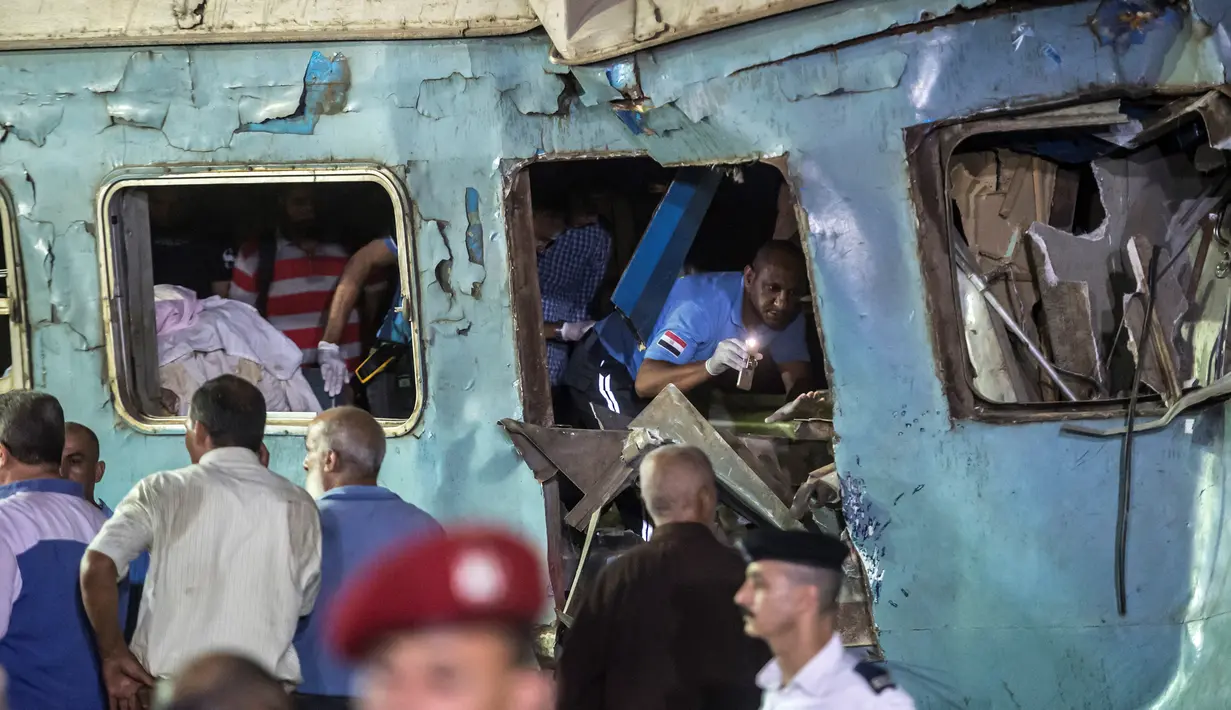 Petugas penyelamat berusaha mencari korban yang terjebak di dalam bangkai kereta usai tabrakan di Kota Alexandria, Mesir (11/8). (AFP Photo/Khaled Deouki)