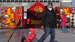 Seorang pria menarik seorang anak melewati dekorasi Tahun Baru Imlek yang dipajang di jalan perbelanjaan pejalan kaki Qianmen, tempat wisata populer di Beijing, Selasa (17/1/2023). Penurunan ini juga diyakini menjadi yang terburuk sejak 1961 yakni tahun terakhir kelaparan hebat di China.  (AP Photo/Andy Wong)