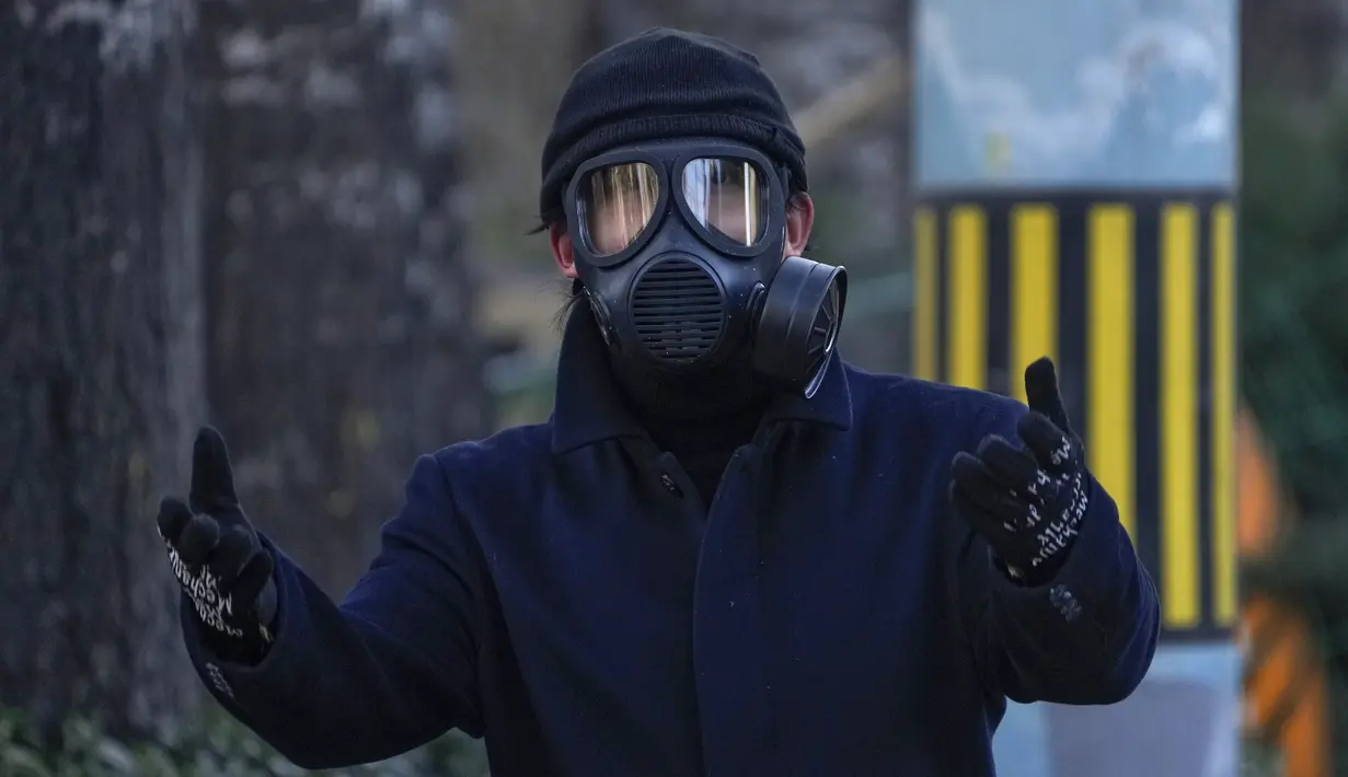 Seorang pria yang mengenakan masker gas memberi isyarat kepada fotografer saat dia berjalan di sebuah jalan di Beijing, Selasa (13/12/2022). Beberapa universitas di China mengatakan akan mengizinkan mahasiswanya menyelesaikan semester dari rumah dengan harapan mengurangi potensi wabah COVID-19 yang lebih besar selama kesibukan perjalanan Tahun Baru Imlek di bulan Januari mendatang. (AP Photo/Andy Wong)