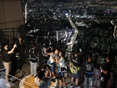 Pengunjung memakai masker untuk melindungi dari penyebaran Covid-19, berselfie saat menginap di lokasi perkemahan semalam di atap gedung pencakar langit di Seoul, Korea Selatan (7/8/2020). Menara Lotte World, setinggi 555 meter gedung pencakar langit dengan 123 lantai. (AP Photo/Lee Jin-man)