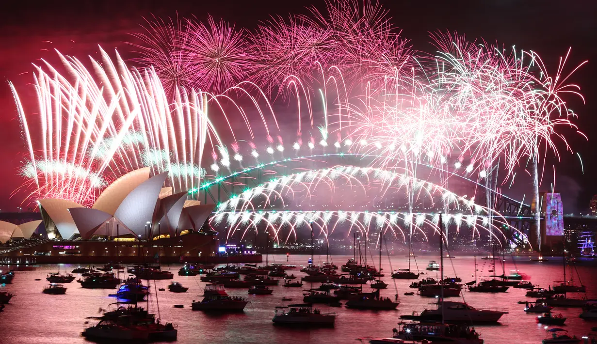 <p>Kembang api Malam Tahun Baru menerangi langit di atas Sydney Opera House (kiri) dan Harbour Bridge saat pertunjukan kembang api di Sydney, Australia pada Minggu (1/1/2022). Malam pergantian tahun identik dengan pesta kembang api. (Photo by DAVID GRAY / AFP)</p>