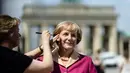 Seorang seniman merapikan dandanan patung lilin Angela Merkel, di depan gerbang Brandenburg di Berlin, (16/7/2014). (AFP PHOTO/Clemens Bilan)