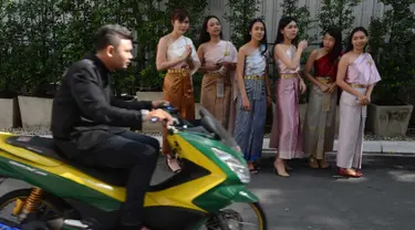 Pengendara motor melintas di depan sejumlah wanita yang mengenakan kostum tradisional setelah upacara agama Buddha sebagai persiapan untuk festival tahun baru Songkran di luar kantor di Bangkok, Thailand (9/4). (AFP Photo/Romeo Gacad)