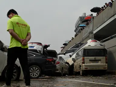 Orang-orang melihat mobil-mobil yang terendam banjir setelah hujan lebat melanda Zhengzhou di provinsi Henan, Kamis (22/7/2021). Henan, provinsi terbesar ketiga di China, yang merupakan rumah bagi sekitar 94 juta orang, telah dilanda badai hujan yang tidak biasa sejak akhir pekan. (Noel Celis/AFP)