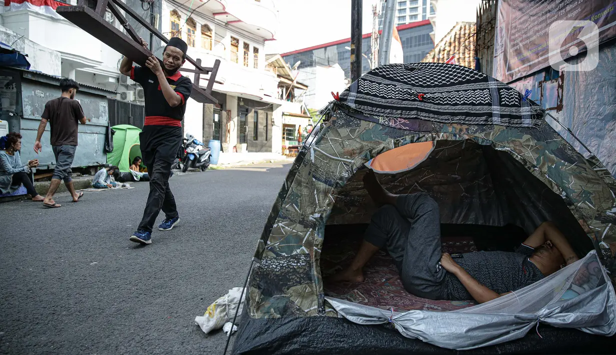 Pejalan kaki melintasi tenda pengungsi Afghanistan di trotoar Kawasan Kebon Sirih, Jakarta, Kamis (26/8/2021). Sebanyak 20 pengungsi asal Afghanistan kembali menempati trotoar dengan harapan bisa diterbangkan ke negara lain dan mendapatkan kehidupan yang lebih layak. (Liputan6.com/Faizal Fanani)