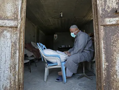 Seorang tukang roti membaca Al-Quran selama bulan suci Ramadan di Kota Gaza, Palestina, Jumat (1/5/2020). (MOHAMMED ABED/AFP)