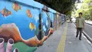 Warga berjalan di samping mural bertema biota laut yang menghiasi dinding di kawasan Cideng, Jakarta, Rabu (29/11/2023). Mural dibuat guna memperindah sekaligus penataan kawasan Kelurahan Cideng, Jakarta Pusat. (Liputan6.com/Herman Zakharia)
