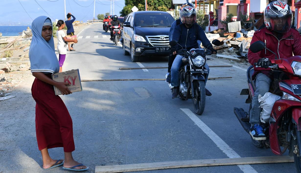 Anak-anak yang terkena dampak gempa meminta sumbangan pada pengguna jalan yang melintas di desa Loli Pesua, Donggala, Selasa (2/10). Akibat terlambatnya pasokan bantuan, mereka terpaksa meminta sumbangan hingga turun ke jalan. (AFP PHOTO / ADEK BERRY)