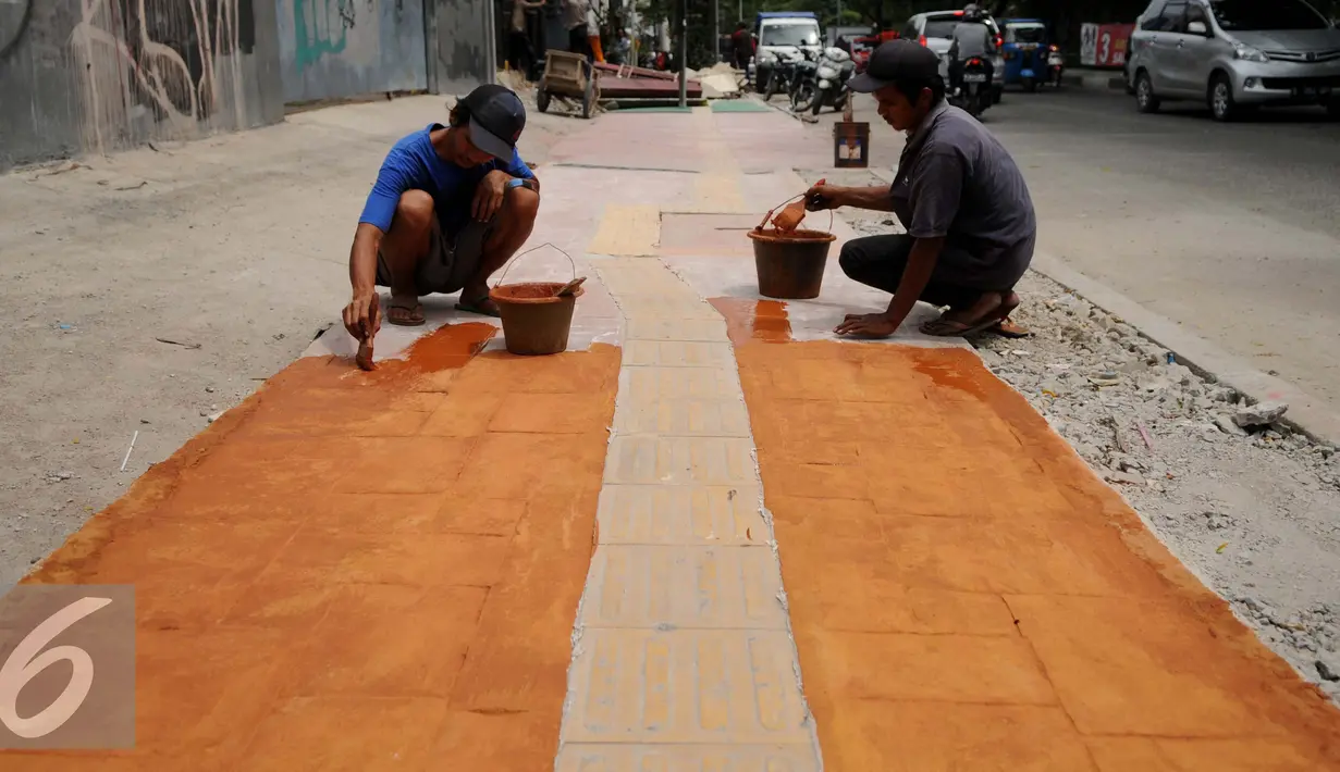 Pekerja sedang mengecat Trotoar Ramah Disabilitas di Jalan Hidup Baru, Kalimati, Jakarta Utara, Selasa (27/12). Pembangunan trotoar ini menggunakan material floor hardener di bagian tengah untuk jalur penyandang disabilitas. (Liputan6.com/Gempur M. Surya)