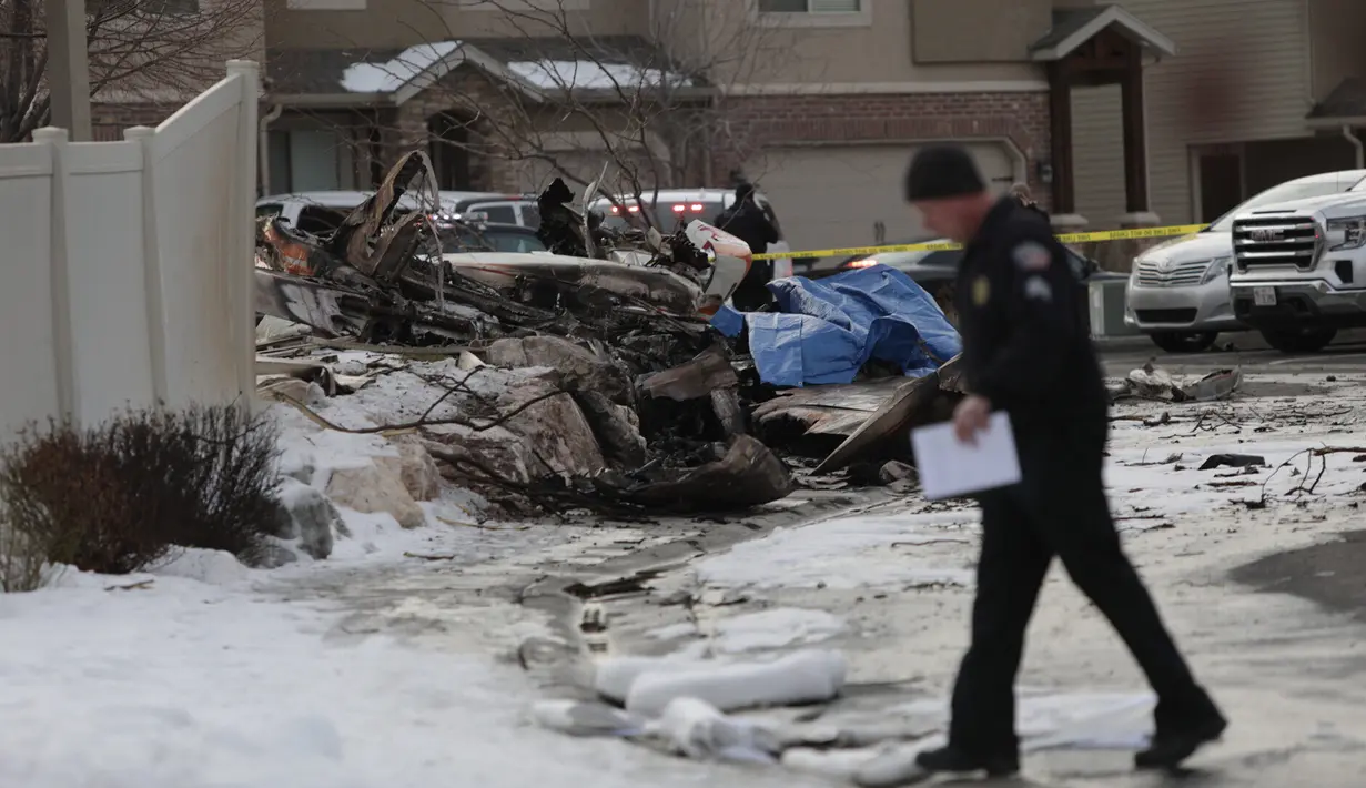 Seorang penyelidik berjalan dekat puing-puing dari pesawat pribadi yang jatuh di kawasan perumahan Roy, Utah, Amerika Serikat, Rabu (15/1/2020). Pesawat bermesin Cessna tersebut terjatuh saat melakukan penerbangan singkat dari Bountiful ke Ogden. (Ben Dorger/Standard-Examiner, via AP)