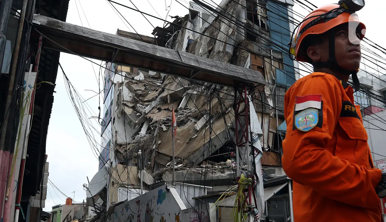Petugas Basarnas berdiri dekat gedung yang ambruk di Jalan Brigjen Katamso, Kota Bambu Selatan, Palmerah, Jakarta Barat, Senin (6/1/2020). Tiga orang dilaporkan terluka akibat tertima material gedung empat lantai tersebut. (Liputan6.com/Johan Tallo)