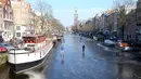 Sejumlah orang berseluncur melintasi permukaan kanal Prinsengracht yang membeku di Amsterdam, Belanda, Jumat (2/3). Cuaca dingin yang melanda Eropa selama beberapa hari terakhir membekukan kanal bersejarah tersebut. (AP/Mike Corder)