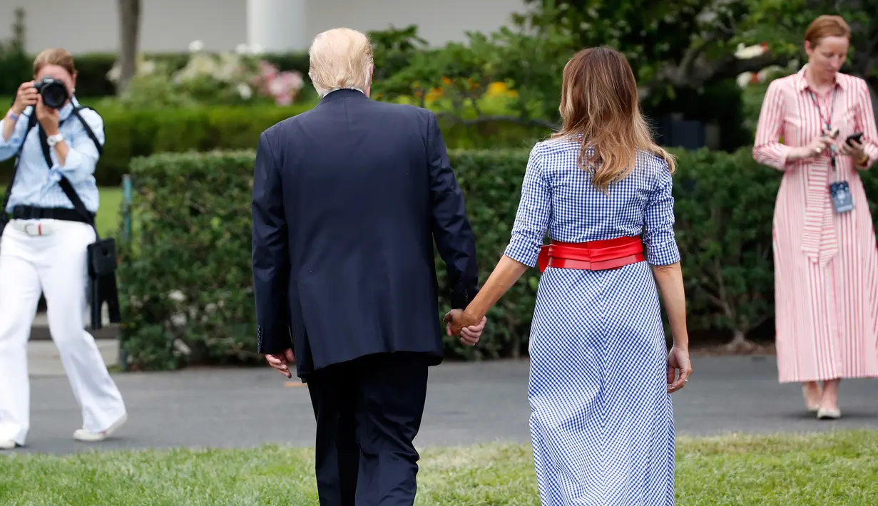 Presiden AS Donald Trump menggandeng tangan istrinya, Melania untuk menyambut keluarga militer pada acara piknik di halaman Gedung Putih, Rabu (4/7). Pasangan yang jarang bergandengan tangan di depan umum itu langsung mencuri perhatian. (AP/Alex Brandon)