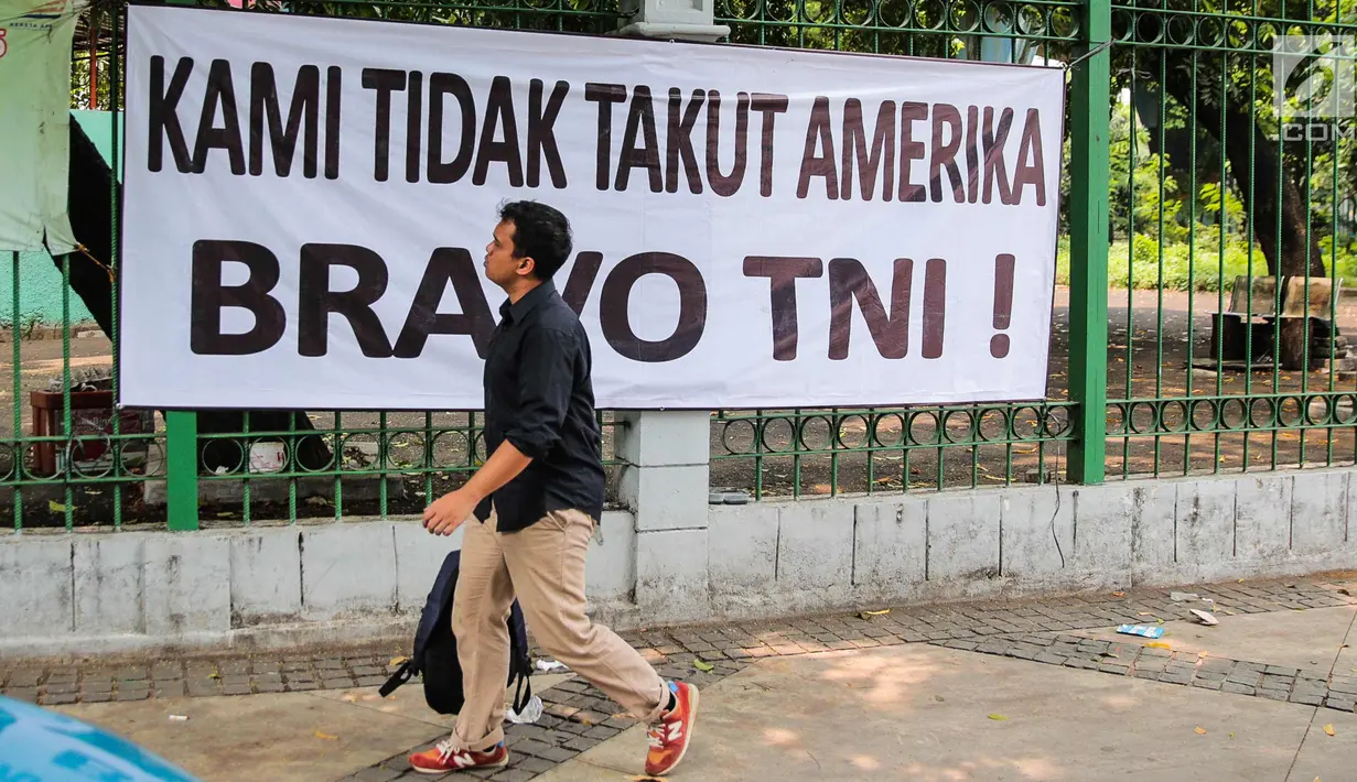 Warga melintas di depan spanduk bertulisan "Kami Tidak Takut Amerika Bravo TNI" terpampang di pagar Stasiun Gambir, Jakarta, Senin (23/10). Pemasangan spanduk ini diduga terkait undangan Panglima TNI yang ditolak masuk AS. (Liputan6.com/Faizal Fanani)