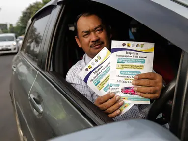 Pengendara mobil menunjukkan selebaran sosialisasi pemberlakuan sistem ganjil genap di pintu masuk Gardu Tol Cibubur 2, Jakarta, Senin (16/4). Kebijakan ini diterapkan untuk mengurai kemacetan di ruas Tol Jagorawi. (Liputan6.com/Faizal Fanani)