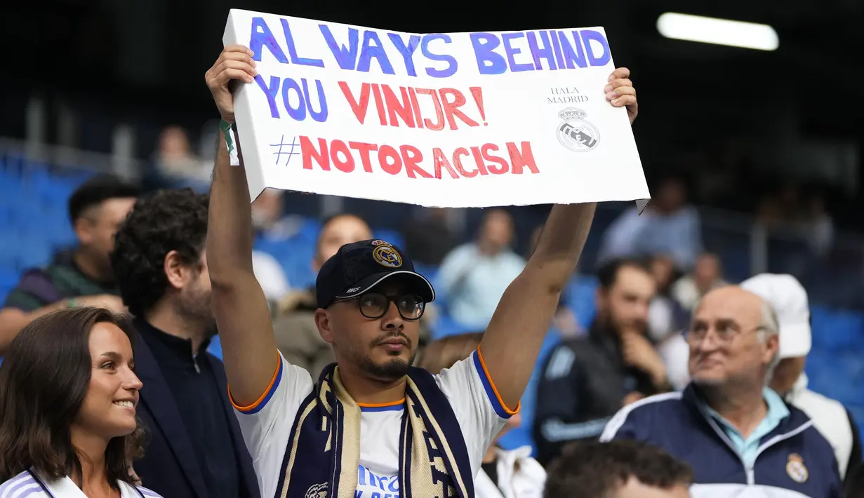 Seorang pendukung Real Madrid membawa poster bertuliskan "Selalu di belakangmu Vini Jr!" pada laga lanjutan Liga Spanyol 2022/2023 antara Real Madrid melawan Rayo Vallecano pada Kamis (25/05/2023) dini hari WIB. Los Blancos memberikan aksi solidaritas sebelum laga tersebut setelah pemain Brasil itu menjadi korban rasisme pada Minggu (21/05/2023) lalu. (AP Photo/Manu Fernandez)