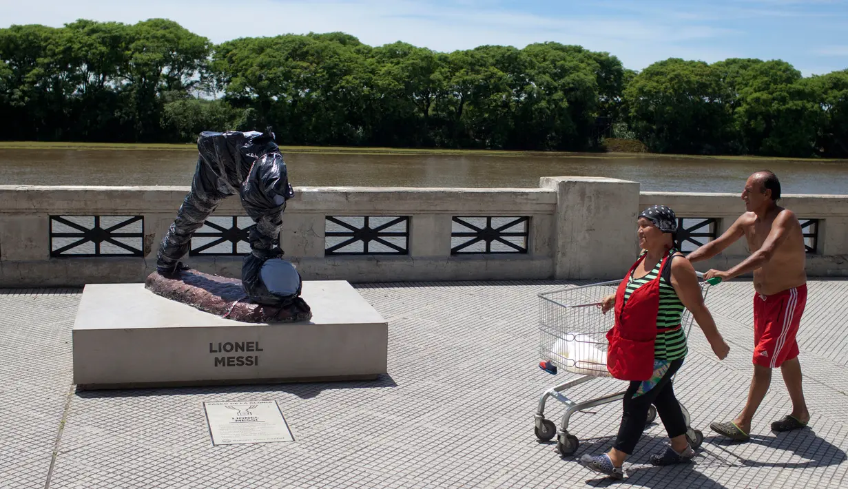 Pejalan kaki mendorong troli belanja dekat patung bintang Argentina, Lionel Messi di Buenos Aires yang dirusak, Selasa (10/1). Patung Messi ini menjadi korban tindakan vandalisme oleh oknum yang tak bertanggung jawab. (AP Photo/Natacha Pisarenko)