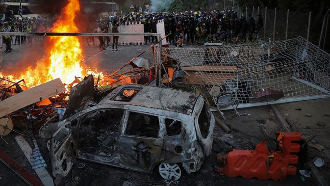 Para pelajar berdiri dekat api dan kendaraan yang hangus terbakar dalam bentrok dengan polisi antihuru-hara di Chinese University, Hong Kong, Selasa (12/11/2019). Gerakan antipemerintah Hong Kong yang telah berlangsung selama lima bulan bertindak semakin keras. (AP Photo/Kin Cheung)