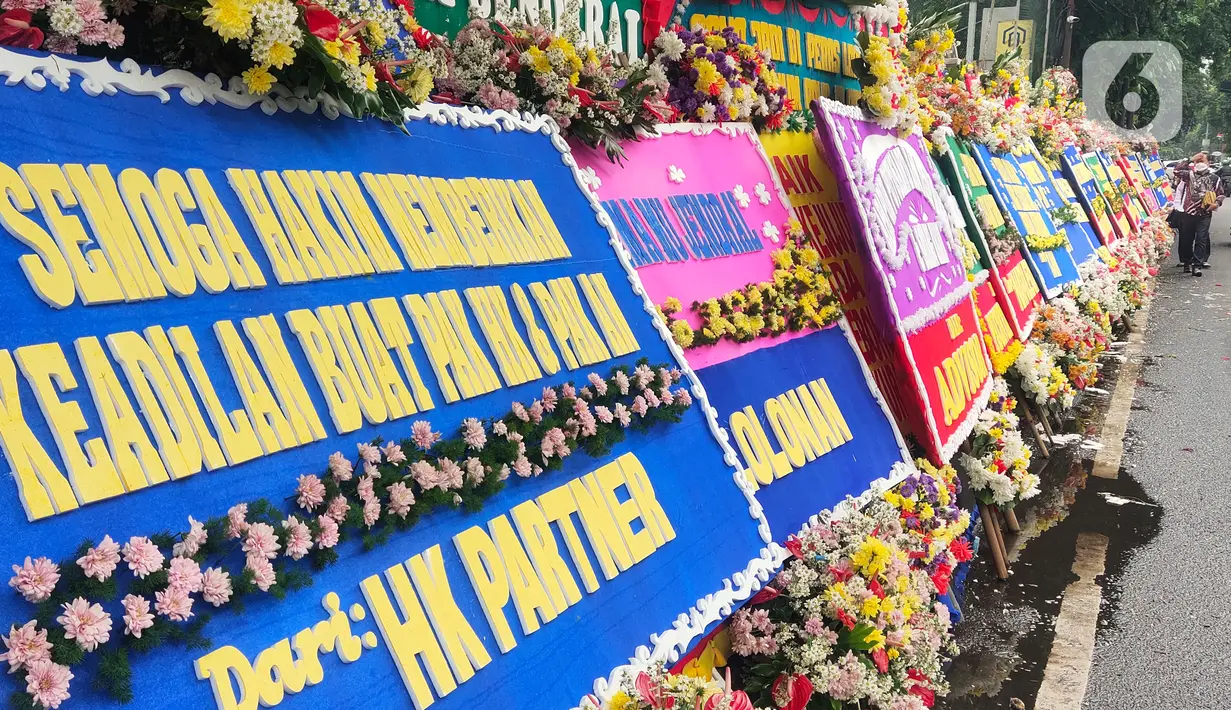 Pejalan kaki melintasi karangan bunga untuk terdakwa Hendra Kurniawan di depan Pengadilan Negeri Jakarta Selatan, Senin (27/2/2023). Karangan bunga itu terus berdatangan dan disusun bertumpuk-tumpuk, bahkan menutupi ruas trotoar yang berada tepat di depan PN Jaksel. (Liputan6.com/Angga Yuniar)