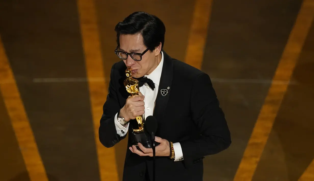 Ke Huy Quan mencium Piala Oscar saat menerima penghargaan kategori Pemeran Pendukung Pria Terbaik di atas panggung Academy Awards ke-95 di Dolby Theatre di Hollywood, California, Minggu (12/3/2023). Ia memulai debut akting di usia yang ke-12 lewat perannya sebagai Short Round dalam film INDIANA JONES AND THE TEMPLE OF DOOM. (AP Photo/Chris Pizzello)