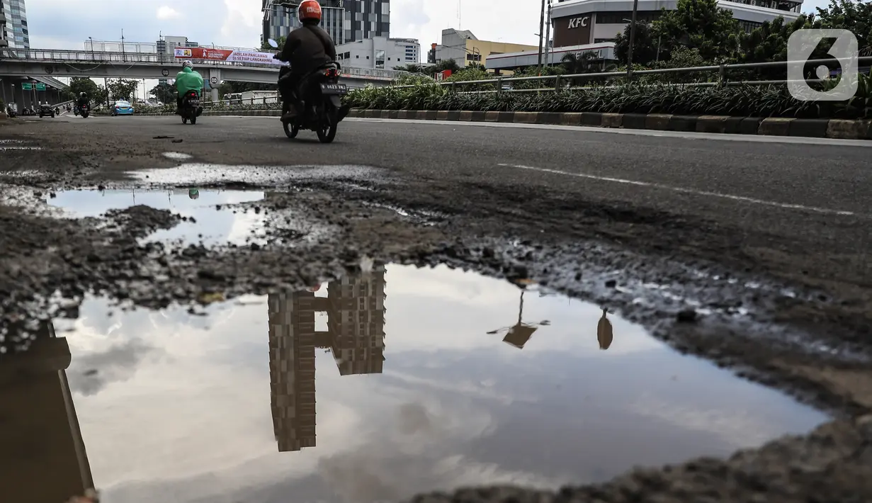 Warga berkendara melintas dekat jalan yang berlubang di kawasan Gatot Subroto, Jakarta, Kamis (18/11/2021). Memasuki musim hujan yang turun hampir setiap hari membuat sejumlah ruas jalan rusak dan tergenang sehingga mengakibatkan jalan berlubang. (Liputan6.com/Johan Tallo)