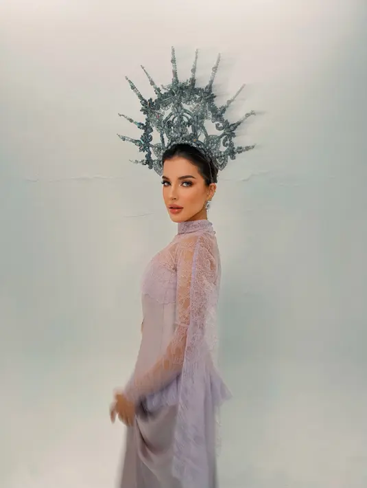 Dari samping, siluet gaun satin yang dililit anggun di bagian rok terlihat jelas. Lengan renda lilac yang menjuntai panjang menambah kesan dramatis, sementara crown silver bergaya halo dengan ornamen filigree dan mutiara membingkai kepalanya. [@tasyafarasya]