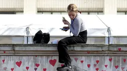 Seorang perempuan makan sambil duduk di atas Tembok Peringatan COVID-19, dengan lukisan hati di seberang Gedung Parlemen, di London, Senin (29/3/2021). Mural hampir 150.000 lukisan hati itu untuk mengenang ribuan orang yang meninggal akibat virus corona di Inggris. (Lucianna Guerra/PA melalui AP)