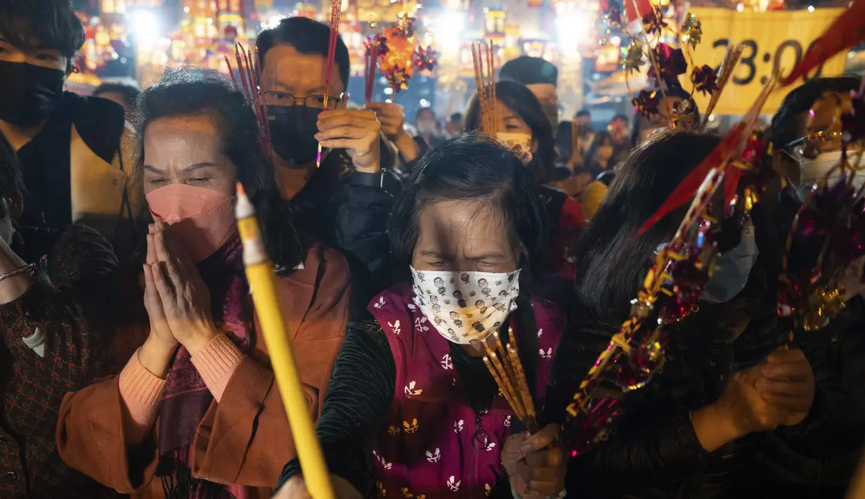 Warga yang mengenakan masker membakar dupa pertama mereka saat berdoa di Kuil Wong Tai Sin untuk merayakan Tahun Baru Imlek yang menandai Tahun Kelinci, di Hong Kong, Sabtu, 21 Januari 2023. Asap dupa memenuhi udara satu jam menjelang Tahun Baru Imlek di Kuil Wong Tai Sin Hong Kong. (AP Photo/Bertha Wang)