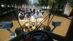 Pekerja mengendarai ekskavator saat membawa para warga menuju kantor di Wuhan, provinsi Hubei, (8/7). Banjir hebat yang belum juga surut membuat warga kesulitan menjalani aktivitasnya. (REUTERS/Stringer)