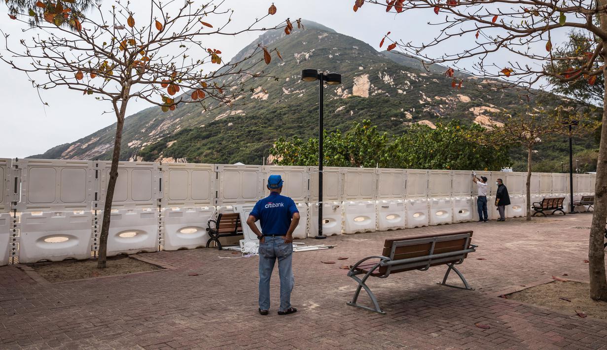 Seorang pria menyaksikan pekerja memasang pagar untuk memblokir akses ke Pantai Shek O di Hong Kong, Kamis (17/3/2022). Pemerintah Hong Kong mengatakan akan menutup pantai umum untuk mengekang penyebaran virus corona COVID-19. (DALE DE LA REY/AFP)