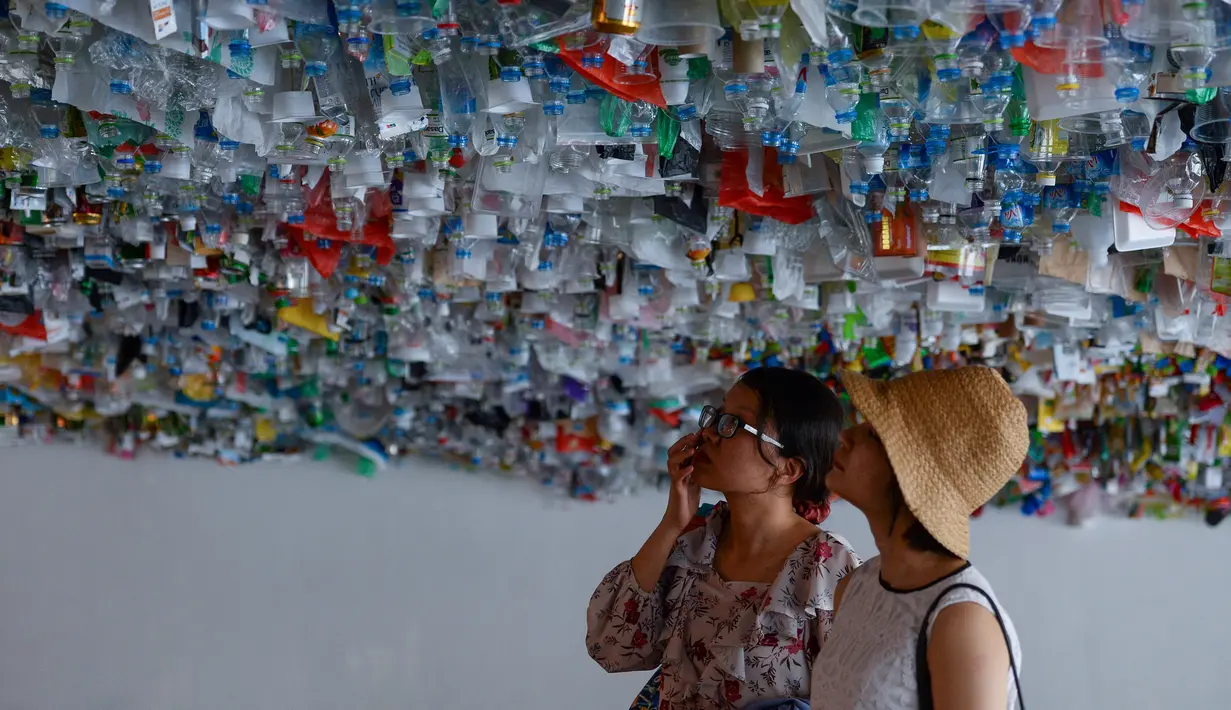 Pengunjung melihat instalasi seni yang terbuat dari sisa-sisa plastik, kaleng dan wadah di sebuah pameran "Reduce the Litter" di Hanoi (15/7/2019). Pameran ini menggambarkan polusi dari limbah rumah tangga yang menyebabkan dampak berbahaya bagi lingkungan dan kesehatan anak. (AFP Photo/Nhac Nguyen)