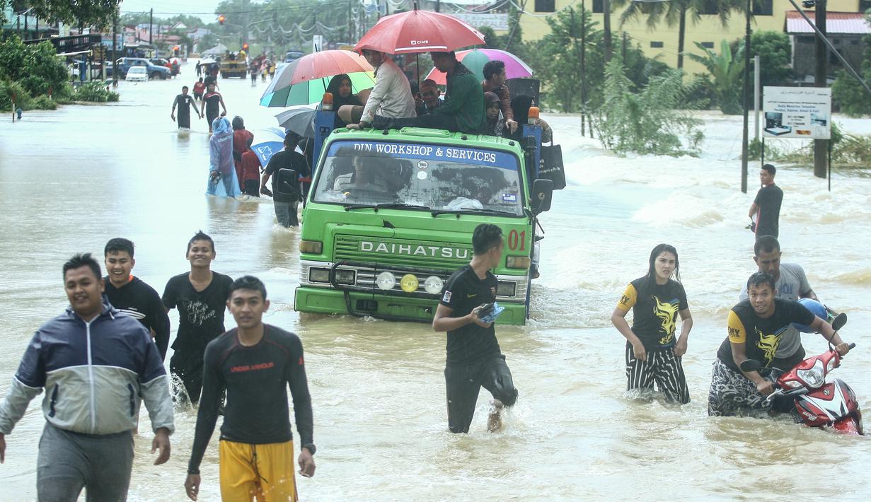 Sejumlah warga menggunakan mobil untuk menerobos banjir di Rantau Panjang, timur laut Malaysia, Selasa (3/1). Akibat hujan lebat yang turun terus menerus selama empat hari di Malaysia, 5.000 warga terpaksa dievakuasi. (AFP PHOTO/STR/Malaysia OUT)