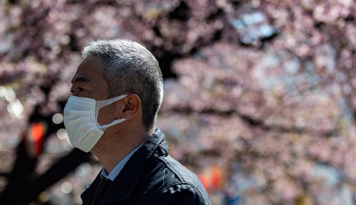 Seorang pria mengenakan masker melewati pohon sakura di taman Ueno, Tokyo (12/3/2020). Hingga Rabu (11/3), Otoritas Tokyo melaporkan 581 kasus, dengan 12 orang meninggal dan 101 sembuh. (AFP/Philip Fong)