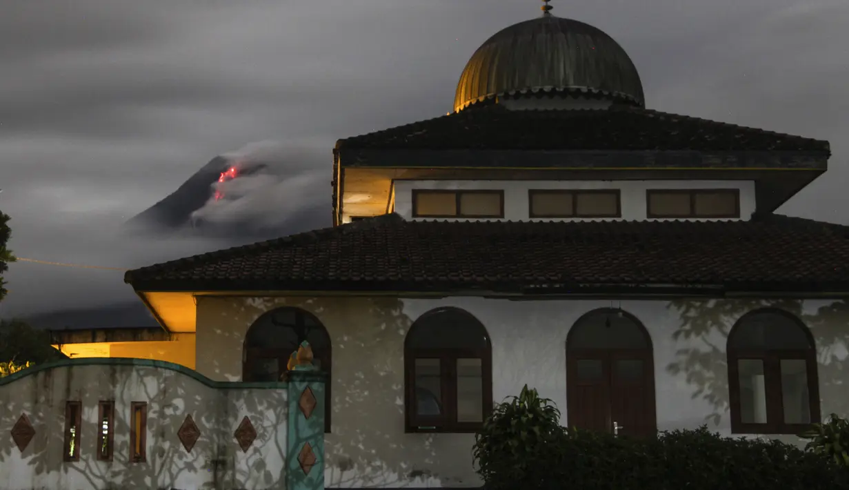 Lava panas mengalir turun dari kawah Gunung Merapi, sebagian terlihat di belakang masjid di Sleman (26/1/2021). BPPTKG mempertahankan status Merapi pada Level III atau Siaga dengan potensi bahaya saat ini berupa guguran lava dan awan panas pada sektor selatan-barat daya. (AP Photo/Slamet Riyadi)